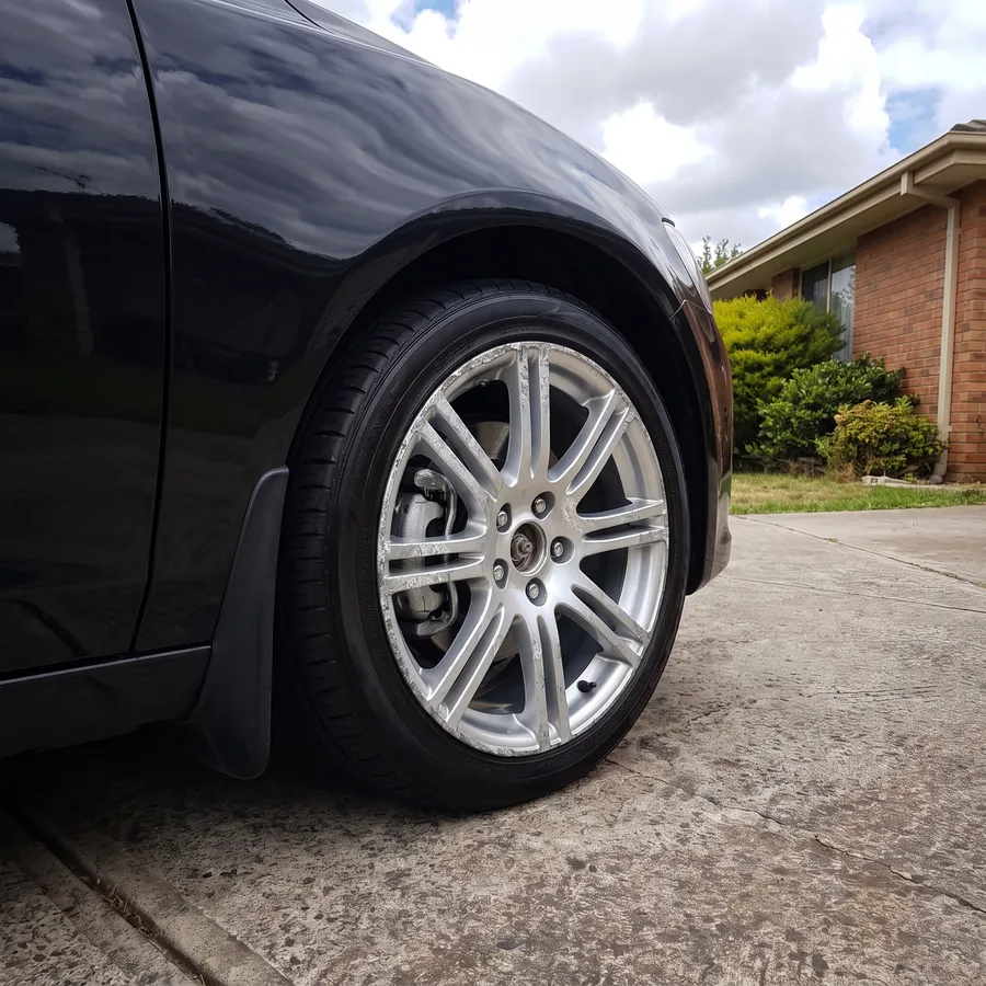 A alloy wheel on a black sedan gouged with kerb rash and corrosion, before the repair