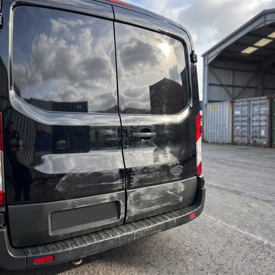 The rear of a black work van, scuffed and scraped across the lower doors and bumper, before the repair
