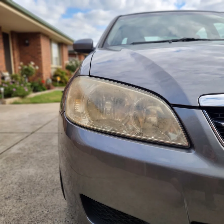 A headlight lens on a grey sedan yellowed, cloudy and oxidised, before the repair